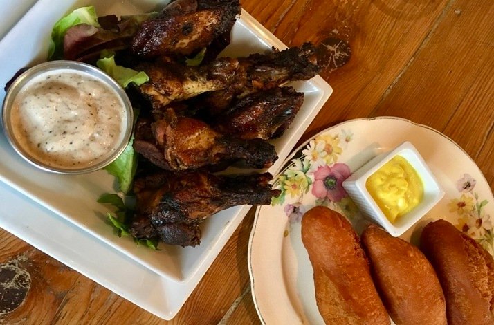 Smoky jerk chicken wings with dipping sauce plated beside golden fried dumplings and mustard on a wooden table at The Edge Harlem.