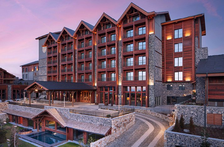Exterior view of Ceylan Splendo'r Uludağ, a luxury mountain hotel with stone and timber architecture, photographed at sunset.
