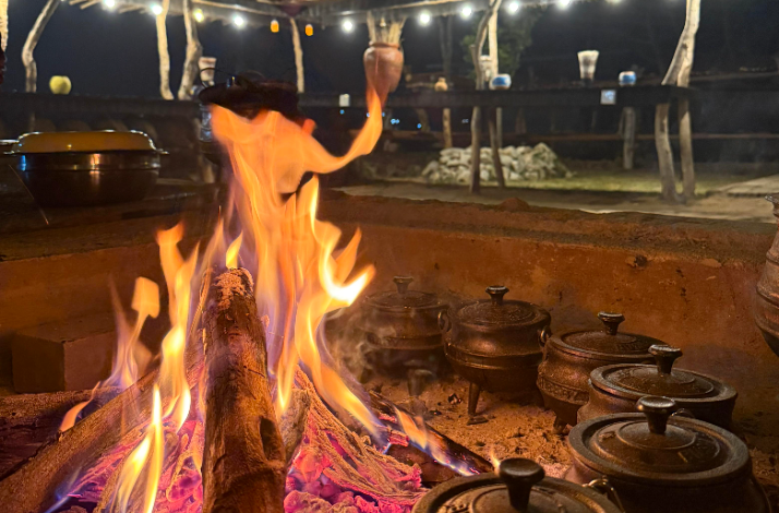 A roaring bonfire warming traditional iron cooking pots at a cultural village in Hazyview.