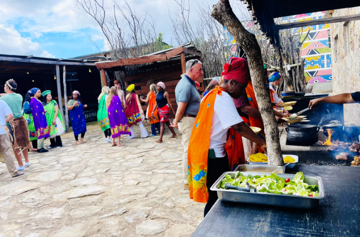 People in vibrant Nguni blankets gathering at a buffet in Hazview, South Africa.