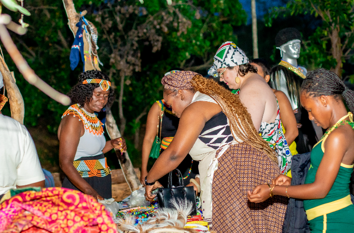  Group of women wearing traditional South African attire examining beadwork and crafts at an open-air cultural stall.