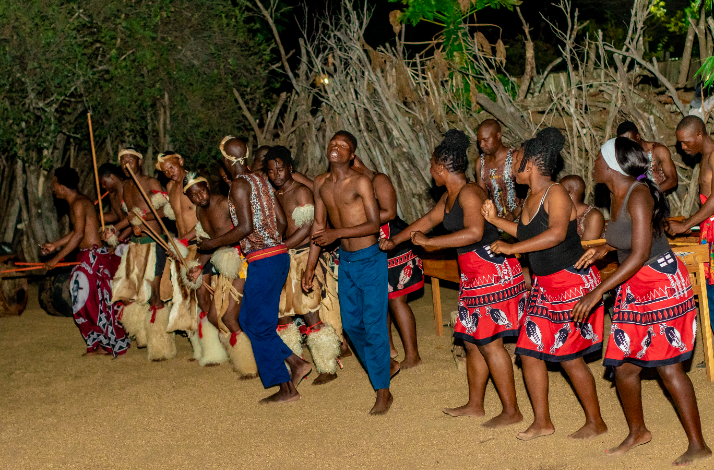 Zulu cultural dancers in traditional attire performing an energetic outdoor night dance at a South African village. 