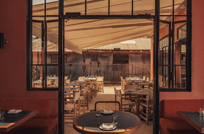 View from inside Loreto restaurant looking out to a shaded outdoor dining area with set tables and rustic decor.