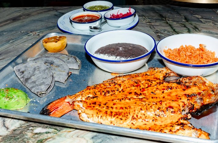 Grilled fish served on a metal tray with black beans, rice, blue corn tortillas, avocado, and assorted salsas in small bowls, served at Loreto.