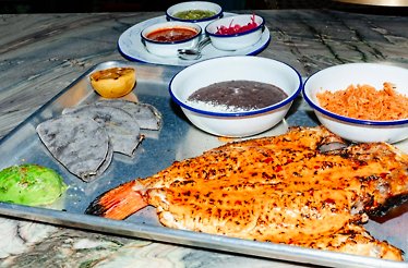 Grilled fish served on a metal tray with black beans, rice, blue corn tortillas, avocado, and assorted salsas in small bowls, served at Loreto.