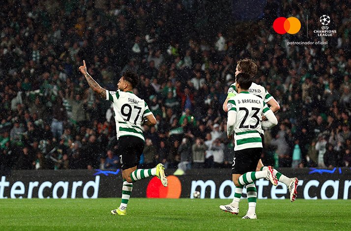Sporting CP's Suarez pointing skyward in celebration alongside D. Braganca during UEFA Champions League Round of 16 second leg.