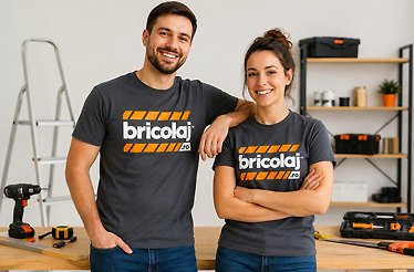  Two smiling people wearing Bricolaj.ro branded grey t-shirts standing in a workshop with tools and shelving in the background.