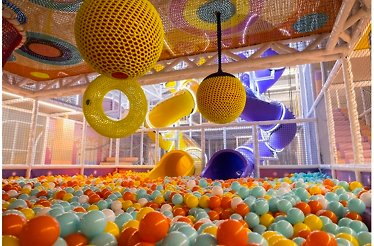 Multi-level Softplay labyrinth at KIDDO featuring yellow mesh ball décor, purple and yellow tube slides, and a colorful ball pit.