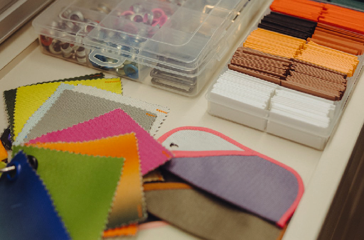 Fabric swatches and a shoe-insole sample on a worktable beside clear organizers holding assorted small parts and neatly stacked color strips.