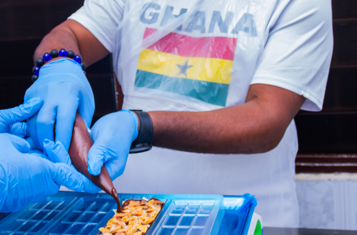 A visitor in a Ghana t-shirt piping chocolate into a bar mold at the '57 Chocolate factory.