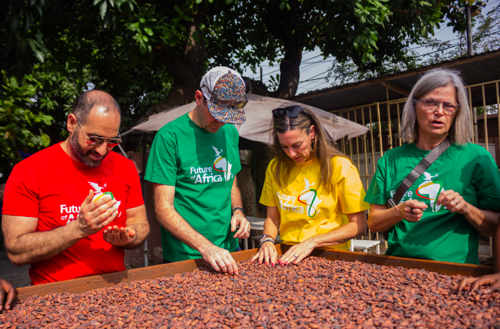 Visitors in colorful t-shirts sorting cocoa beans outside the '57 Chocolate factory in Accra.