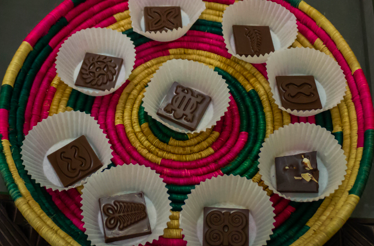 A colorful woven basket filled with '57 Chocolate pieces decorated with traditional Ghanaian Adinkra symbols.