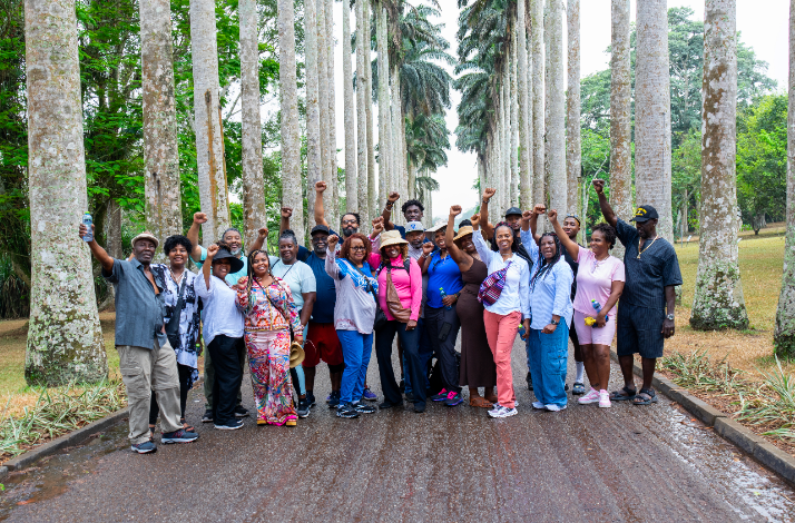 A tour group posing with raised fists under tall palm trees at the Aburi Botanical Gardens in Ghana.