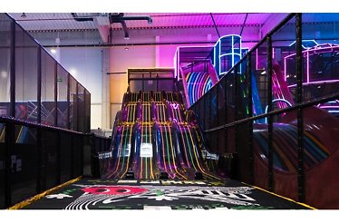 Towering neon-striped indoor slide at Hype Play glowing in pink and yellow, framed by dark mesh safety enclosures.