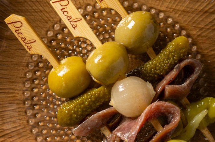 Picala's signature pintxos skewers with olives, gherkins, and anchovies, served in a dimpled glass dish.