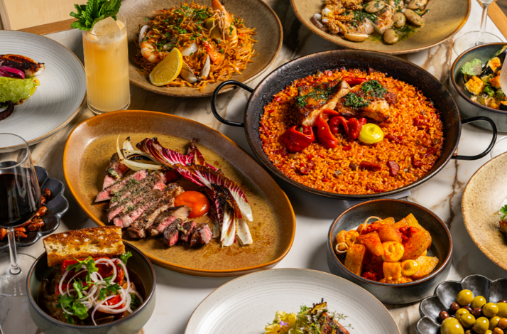 Picala's full table spread showcasing paella, grilled meats, olives, anchovies, and vibrant cocktails.