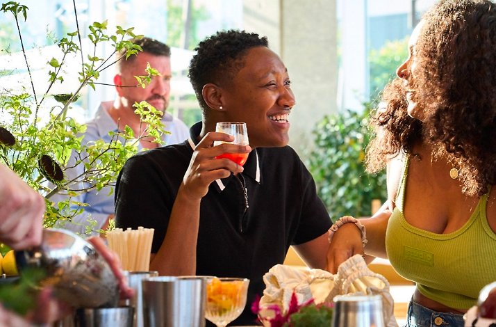 Guests socializing and holding cocktails at Picala's lively bar area, surrounded by fresh greenery and citrus.