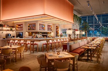 Picala's warmly lit dining room at night, featuring a central bar, long banquettes, and floor-to-ceiling windows.