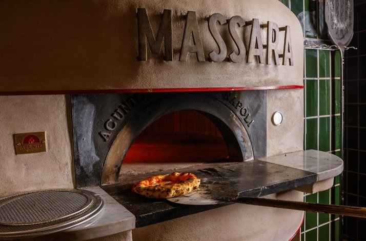 Massara's wood-fired oven with a freshly baked pizza resting on the stone hearth, framed by green tiles.