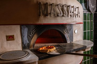 Massara's wood-fired oven with a freshly baked pizza resting on the stone hearth, framed by green tiles.