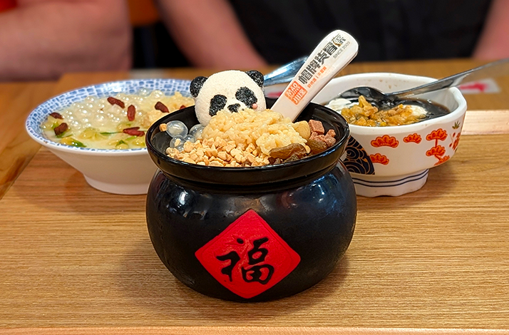 Panda-topped dessert in a black jar with a red “Fu” label, served with two bowls on a wooden tray.
