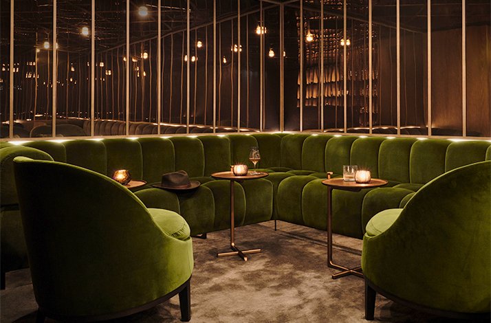 Intimate bar at The Londoner featuring green velvet booths, pendant lighting, and glasses arranged for a whisky tasting.