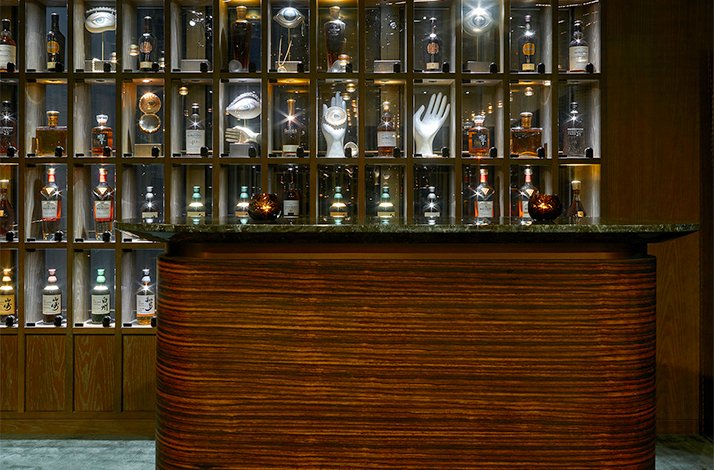 Curated whisky collection on illuminated shelves behind a striped wood bar counter at The Londoner, London.