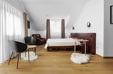 Bright, modern double room at Hotel Piatra Șoimului, Sinaia, with sloped ceiling, leather armchair, and natural wood flooring.