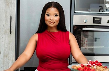 Chef Black posing confidently in a professional kitchen, wearing a red top, with a Whirlpool oven and a dessert plate in the foreground.
