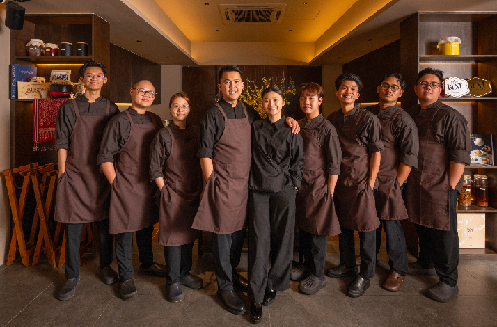 Akar restaurant's kitchen team posing together in brown aprons and black uniforms inside the warmly lit dining room.
