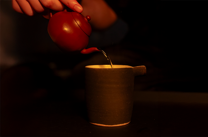 Tea being poured from a red clay teapot into a handcrafted ceramic cup during a contemporary tea ceremony.