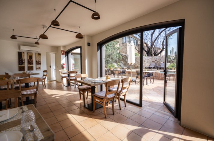 Bright, modern dining area with wooden chairs and set tables, opening onto an outdoor patio through arched sliding doors.