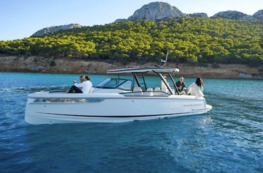 A sleek white motorboat with a few passengers rides on calm turquoise water near a forested shoreline and mountain.