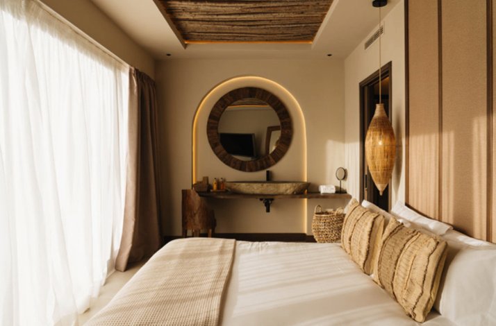 Warm, modern bedroom with a large bed, floor-to-ceiling curtains, and a round backlit mirror above a vanity.