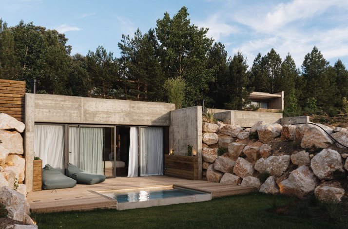 Concrete suite with sliding glass doors opening to a small private pool and deck, bordered by large rocks and greenery.
