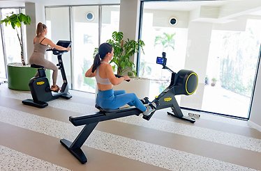 Two women working out at Nelumbo Med-SPA fitness area, one using a rowing machine, one on a stationary bike.