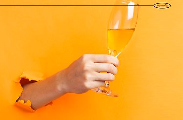 Hand holding a glass of white wine, emerging through a torn orange paper background.