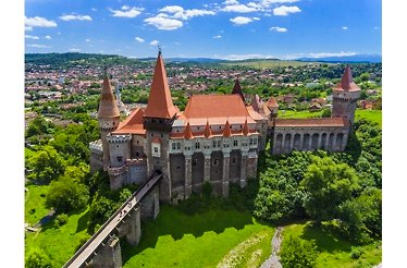 Aerial view of Corvin Castle in Hunedoara, Romania, with Gothic towers, stone bridge, and green surroundings.