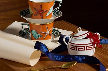 Orange Ginori 1735 porcelain teacup set with starfish print, paired with a red Greek-key sugar bowl and branded satin ribbon.