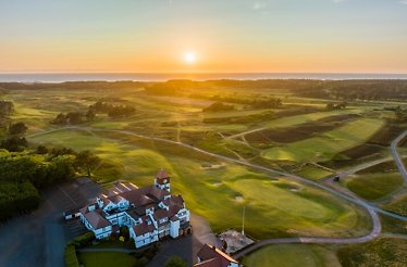 Drone shot over Formby Golf Club's parkland-links layout at dusk, clubhouse centred with golden light reflecting off the coastal horizon.