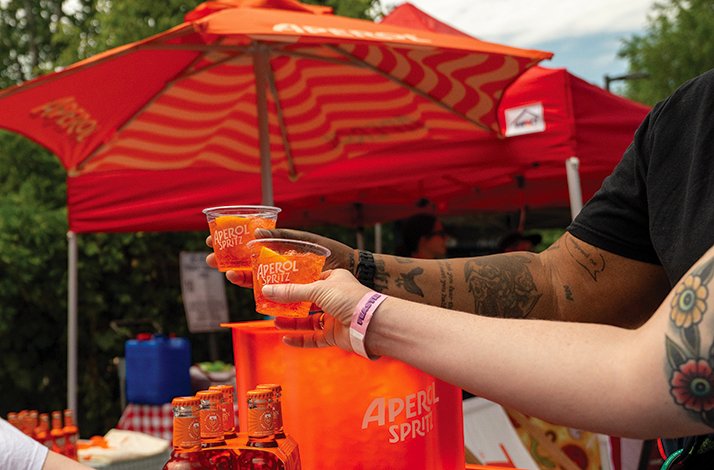 Aperol Spritz cocktails being served at a branded festival booth.