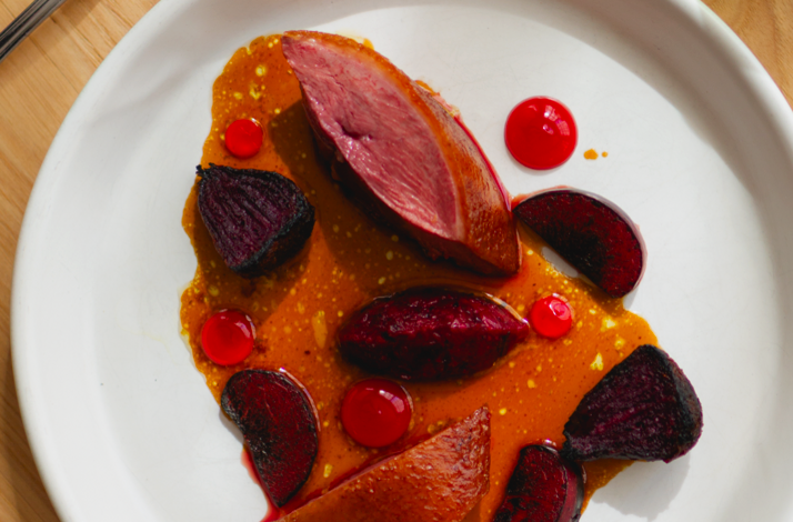 A dish of sliced duck breast, roasted beets, and glossy red sauce dots on a white plate served at Firstborn.