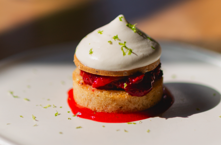 Dessert plate at Firstborn with a small layered cake, cherries, bright red sauce, and a dome of whipped cream.