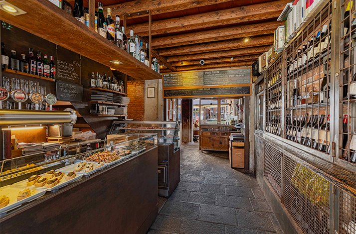 Traditional Venetian bacaro bar at Osteria Bancogiro with cicchetti counter, ceiling wine bottles, and chalkboard wine list.