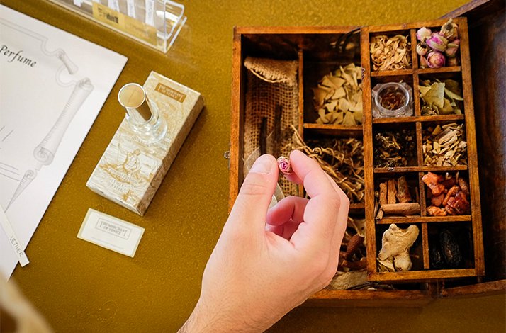 Workshop desk displaying natural scent materials in a compartment tray, perfume bottle, and 'My Perfume' blending worksheet.
