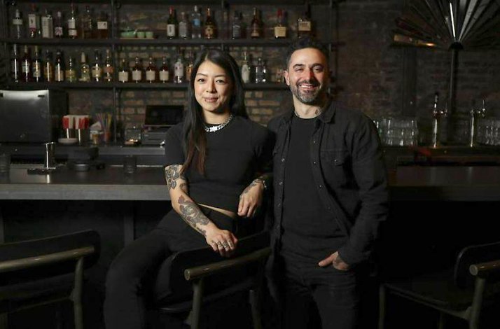 Lily Wang and Joe Briggs of Nine Bar smiling together, posed in front of a bar stocked with spirits.