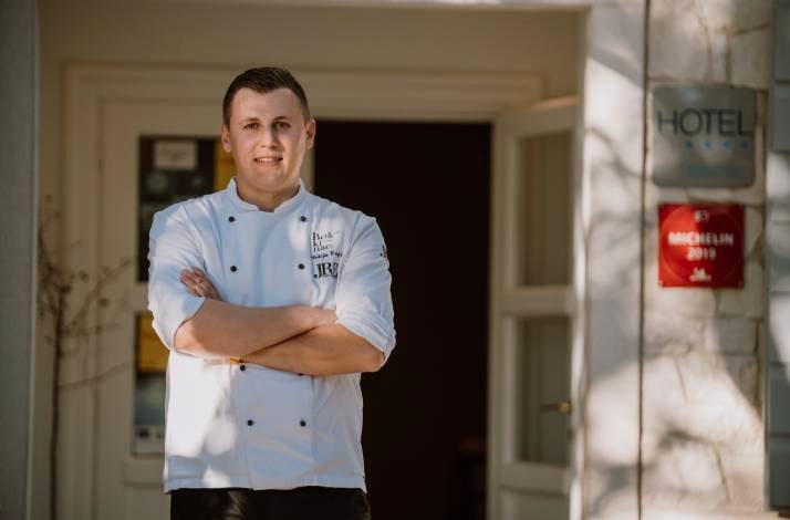 Chef in a white jacket standing outside the restaurant entrance.