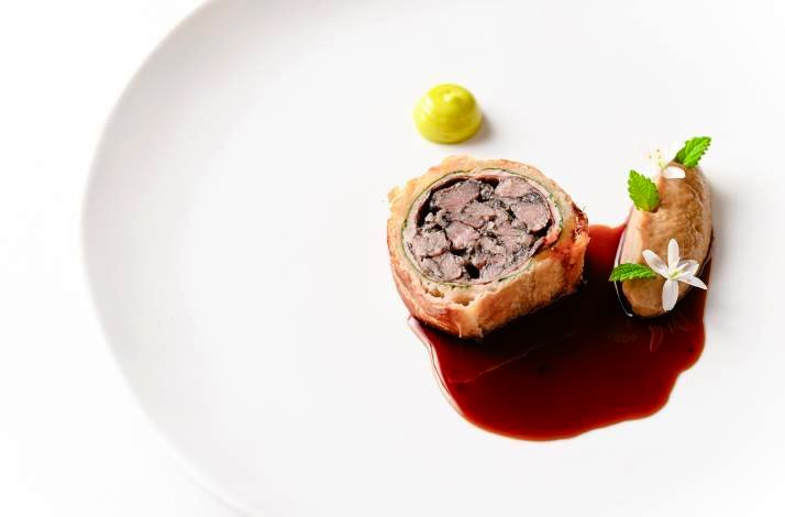 Elegant plated course with a roulade-style centerpiece and rich sauce on a white plate.