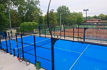 Elevated view of blue padel courts at North Padel in Herăstrău Park, enclosed by glass walls and surrounded by lush trees.