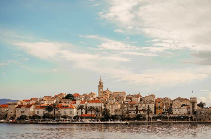 Panoramic view of Korčula Old Town's medieval stone skyline rising above the Adriatic, with a bell tower and terracotta rooftops.